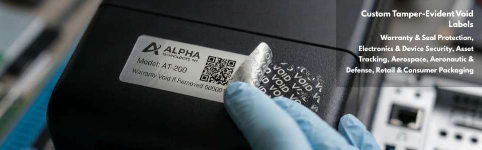A gloved hand peels back a tamper-evident security label from a black electronic device, revealing a repeating VOID pattern on the surface beneath, demonstrating Intertronixs tamper-evident label technology for electronics, aerospace, and defense 